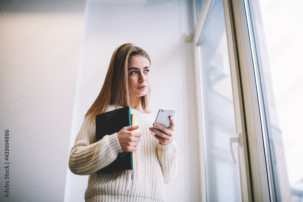 Dreamy young lady using cellphone and looking out window Dreamy young lady using cellphone and looking out window