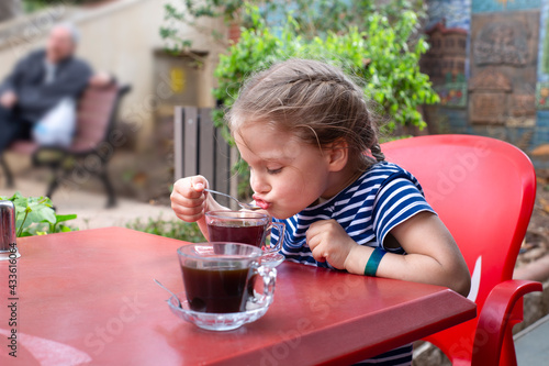 Child girl sitting at the table sips hot tea from a teaspoon photo