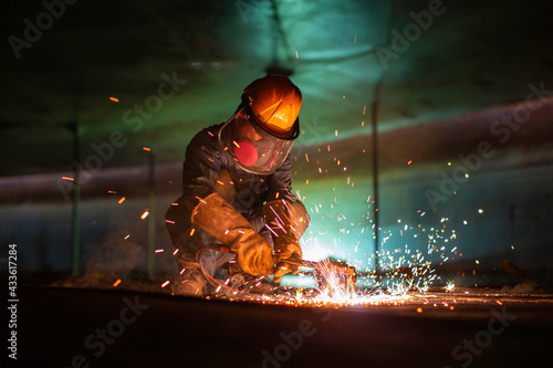 Male worker metal cutting spark on tank bottom steel plate with flash of cutting light close up wear protective gloves and mask