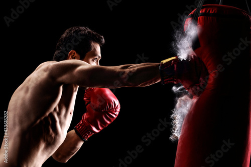 Strong muscular man punching a bag with boxing gloves