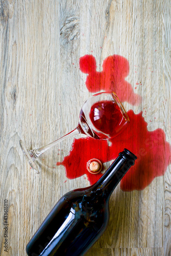 a bottle of wine and a glass lie on the wooden floor, spilled red wine, top view