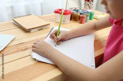 Little girl drawing on paper with pencil at online lesson indoors, closeup. Distance learning