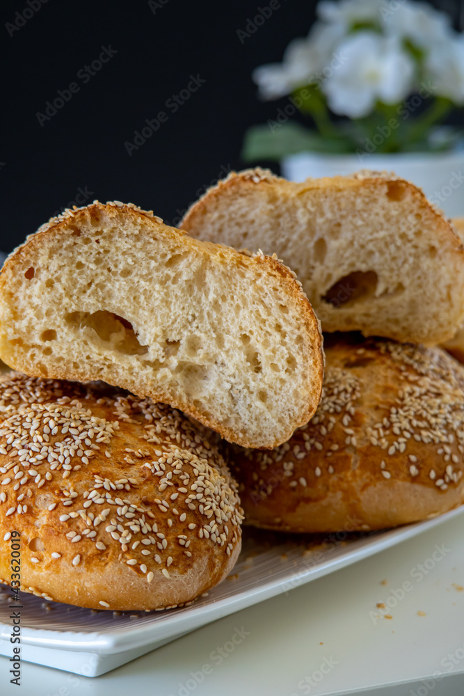 Fresh challah bread rolls hot from the oven cut into half. Crumb shot of gluten free bread buns or mini loaves with sesame seeds and golden color. Fluffy homemade bread, dark background with flowers Fresh challah bread rolls hot from the oven cut into half. Crumb shot of gluten free bread buns or mini loaves with sesame seeds and golden color. Fluffy homemade bread, dark background with flowers