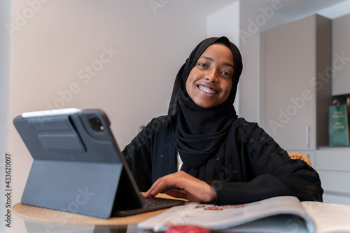 Black Muslim teenage girl doing work on a small electronic device 