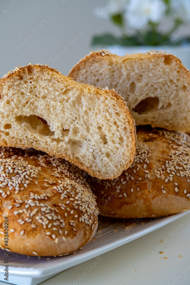 Fresh challah bread rolls hot from the oven cut into half. Crumb shot of gluten free bread buns or mini loaves with sesame seeds and golden color. Fluffy homemade bread, white background with flowers