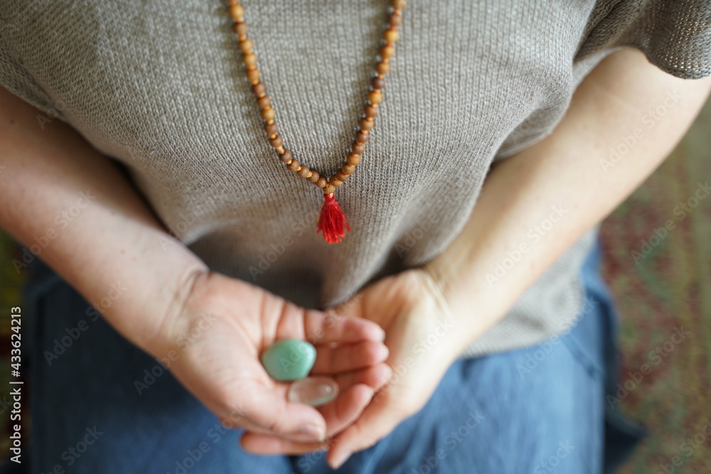 hands of a woman holding stones with upper body wearing a mala 
