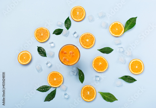 Fresh orange juice in glass with sliced oranges and ice on blue background.