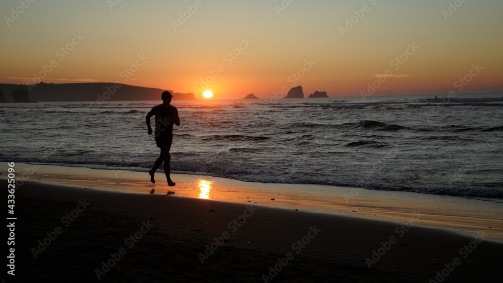 person running on the beach at sunset, valdearenas beach, liencres, cantabria, north spain