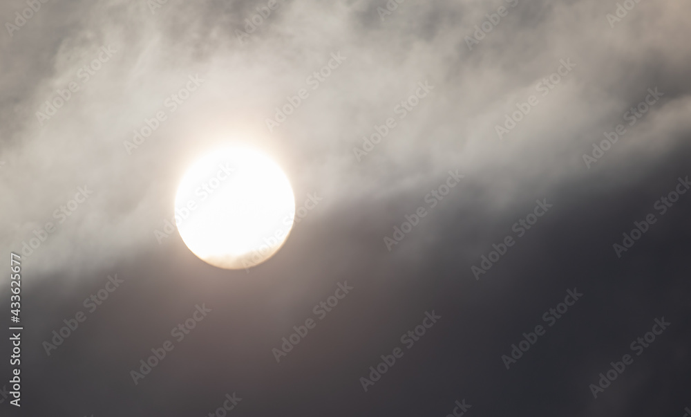 The sun shines behind the clouds during