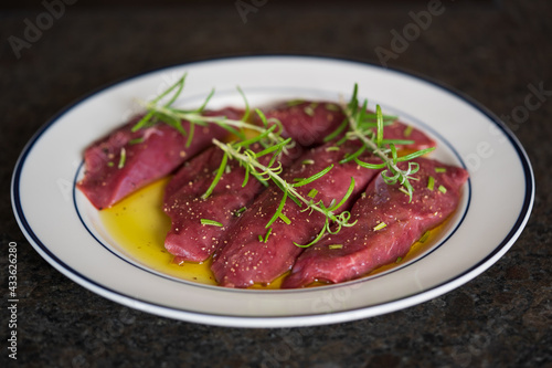 cooking at home - fresh meat from a red deer calf for grilling on a plate with olive oil and herbs