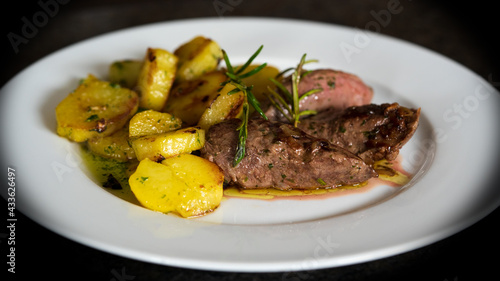 ready to eat, roasted meat from a red deer calf with roasted potatoes on a white plate