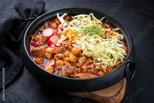 Traditional slow cooked Mexican pozole rojo soup with pork meat and hominy maiz served as top view in a modern design cast-iron roasting dish on an old rustic wooden board photo