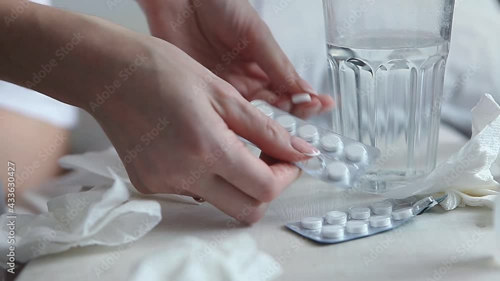 A young woman feels cold in a bed. Human hands take out a pill from the package and take a glass of clean water, taking medicine, close-up. Fever concept. A young woman feels cold in a bed. Human hands take out a pill from the package and take a glass of clean water, taking medicine, close-up. Fever concept.