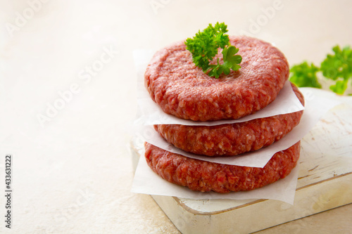 Cooking homemade burgers. Stack of raw red meat cotlets on bright background.
