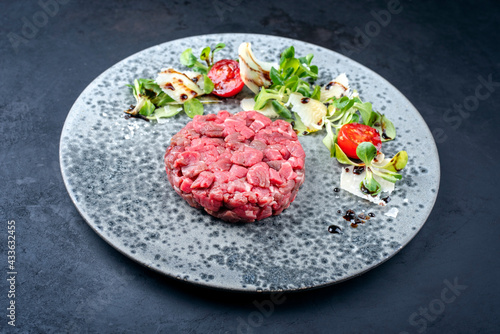 Modern style gourmet tartar raw from beef filet with lettuce, tomatoes and parmesan as close-up on a Nordic design plate with copy space
