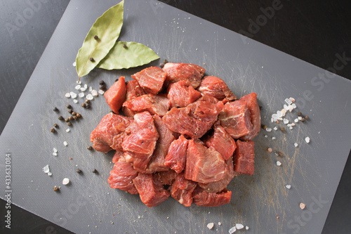 Raw beef of veal cut into cubes on a gray cutting board next to bay leaves, black pepper peas and coarse salt. Ingredients for making a delicious home-made meal photo