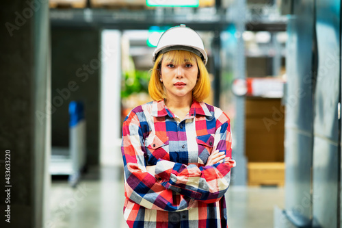 Female staff with helmet is standing in warehouse.