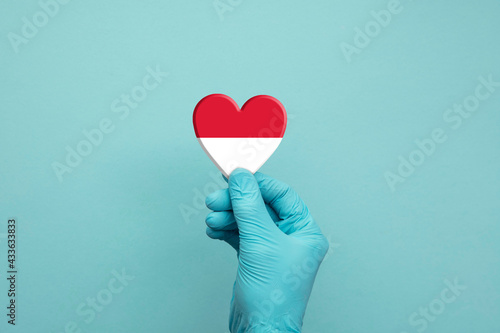 Hands wearing protective surgical gloves holding Indonesia flag heart