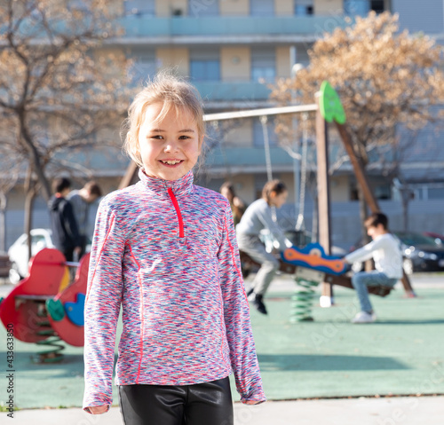 Portrait of small smiling girl standing on outdoors playground at sunny day