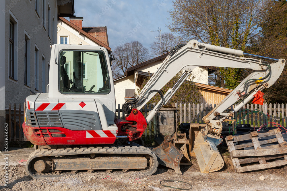 Obraz premium Abgestellter kleiner Bagger mit breiter Baggerschaufel in der Seitenansicht auf einer Baustelle