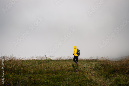 Tourist walking at meadow in wind and bad weather. Hike in mountains during overcast. Woman wearing waterproof sports clothing