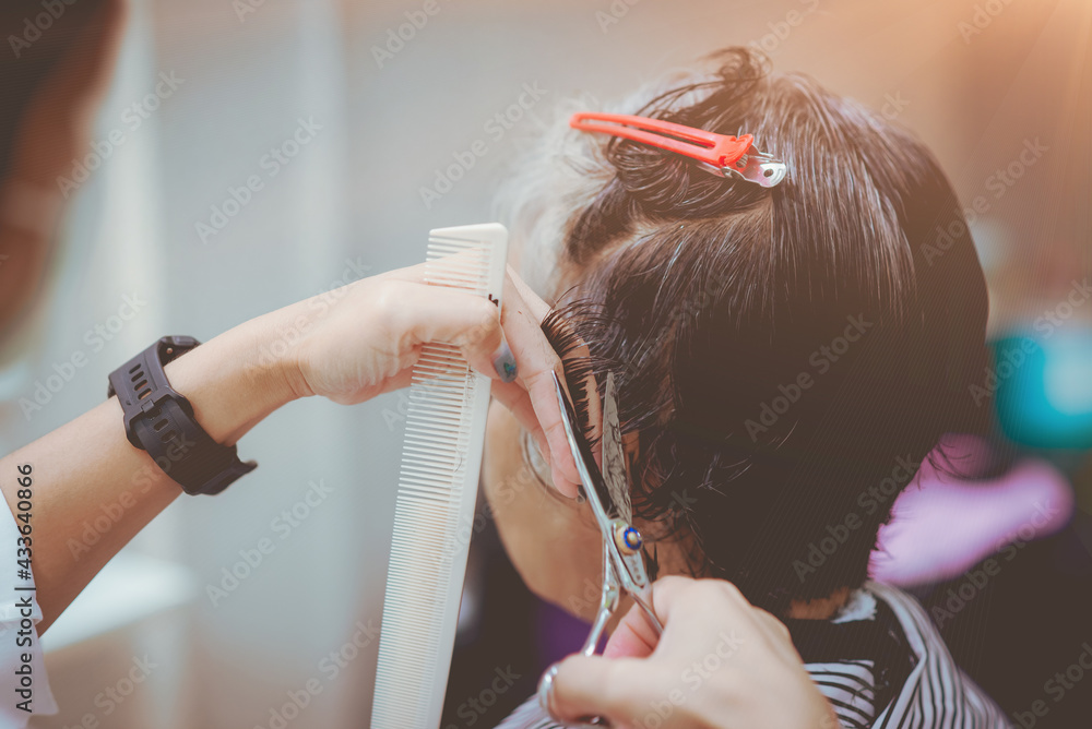 Fototapeta premium Asian woman barber wears green mask cut black, white hair old customer. beautiful hairstylist trimming with scissors in haircut. female Hairdresser working in Thai stylist beauty salon