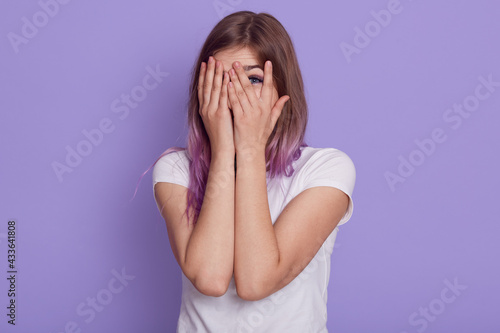 Φωτογραφία Attractive young woman wearing white casual t shirt covering her face with palms and looking through fingers, spying for somebody, isolated over purple background