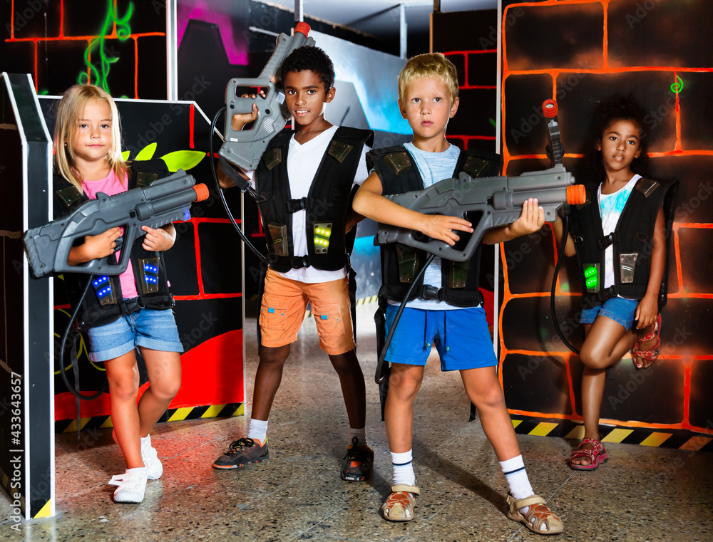 Joyful teens aiming laser guns at other players during lasertag game in dark room. High quality photo