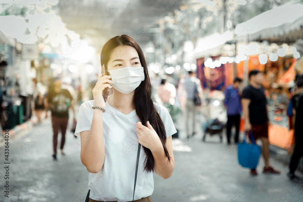 beautiful asian woman wear white mask to protect against dust PM 2.5 and viruses when going out for shopping in Thailand. pretty girl use mobile phone in outdoor.soft focus and blurry background
