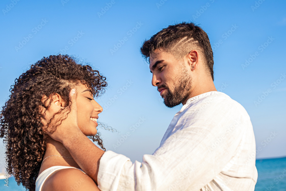 Moment of tenderness between young multiracial couple of happy lovers who look into each other's eyes while he smilingly holds her head in hands. Passion and love of two Latin people on sea vacations Moment of tenderness between young multiracial couple of happy lovers who look into each other's eyes while he smilingly holds her head in hands. Passion and love of two Latin people on sea vacations