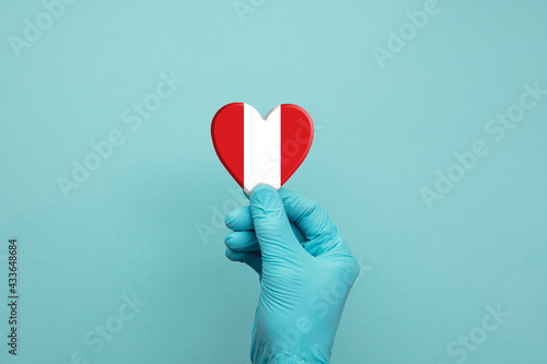 Hands wearing protective surgical gloves holding Peru flag heart
