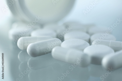 On a glass table lies a plastic bottle with medical pills scattered near