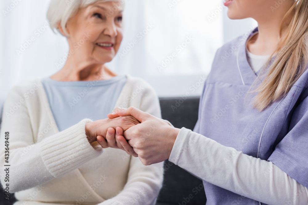 Fototapeta premium nurse holding hand of aged woman smiling on blurred background