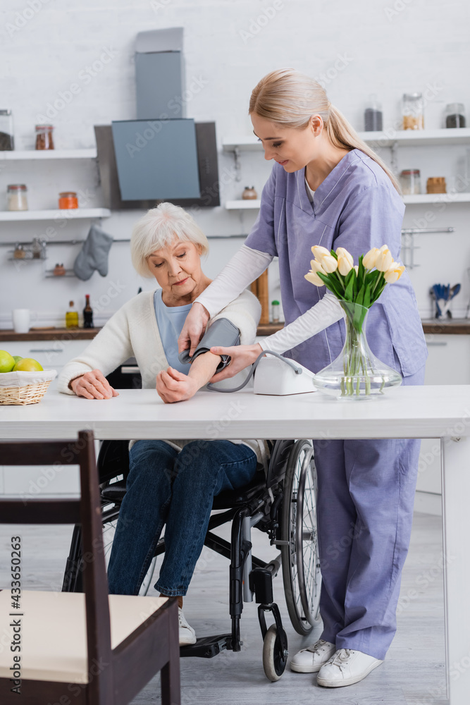 young nurse measuring blood pressure of handicapped woman in wheelchair at home