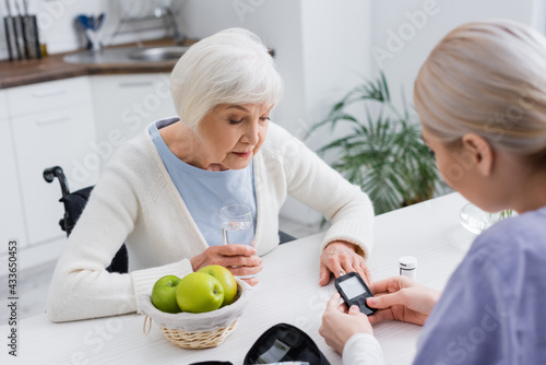 senior woman looking at glucometer in hands of nurse on blurred foreground