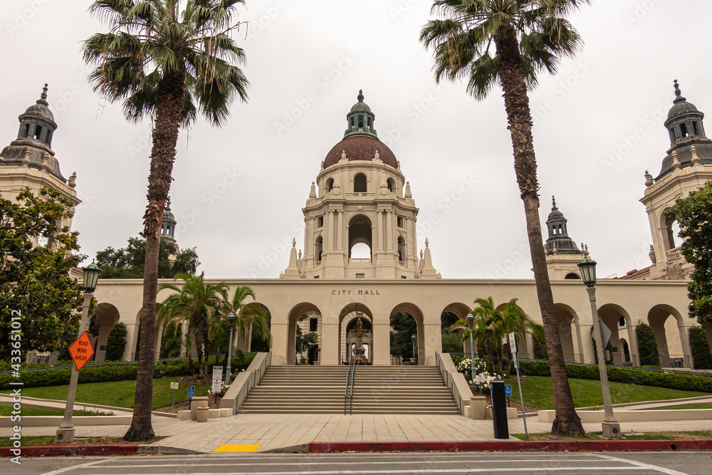 Pasadena, CA, USA - May 11, 2021: North Euclid ave view of beige stone  back side with main and side towers and dome of historic City Hall under silver sky. Palm trees and other green foliage.