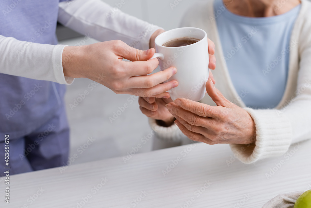 cropped view of social worker giving cup of tea to senior woman, blurred background cropped view of social worker giving cup of tea to senior woman, blurred background