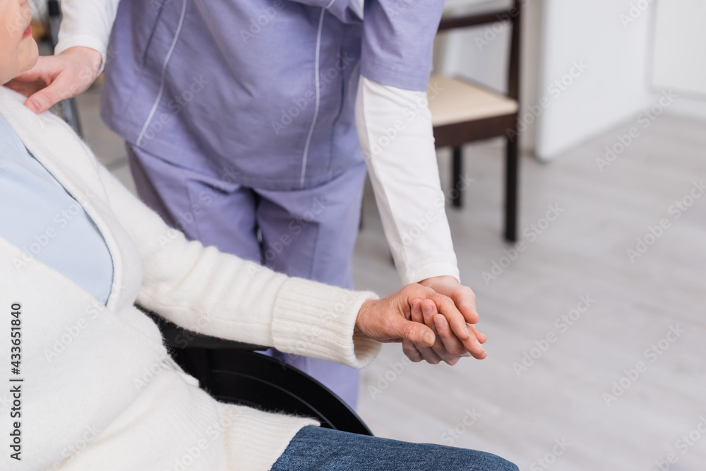 Fototapeta premium partial view of social worker holding hand and touching shoulder of senior handicapped woman