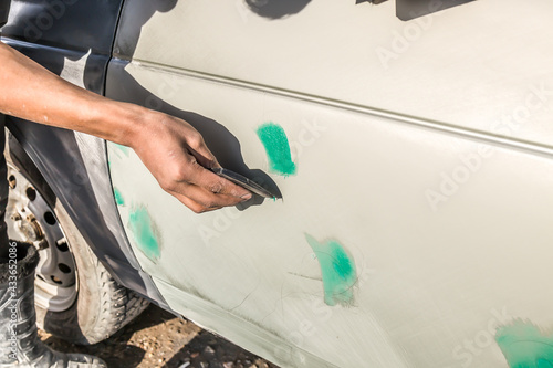 Car repair after an accident. Putting putty on the metal surface of the car. Body work.