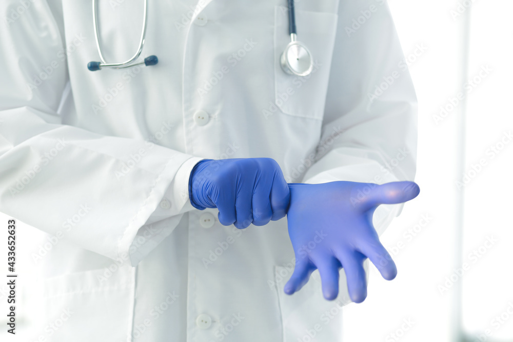 Doctor with medical stethoscope in a medical gown puts on protective gloves in a hospital Doctor with medical stethoscope in a medical gown puts on protective gloves in a hospital