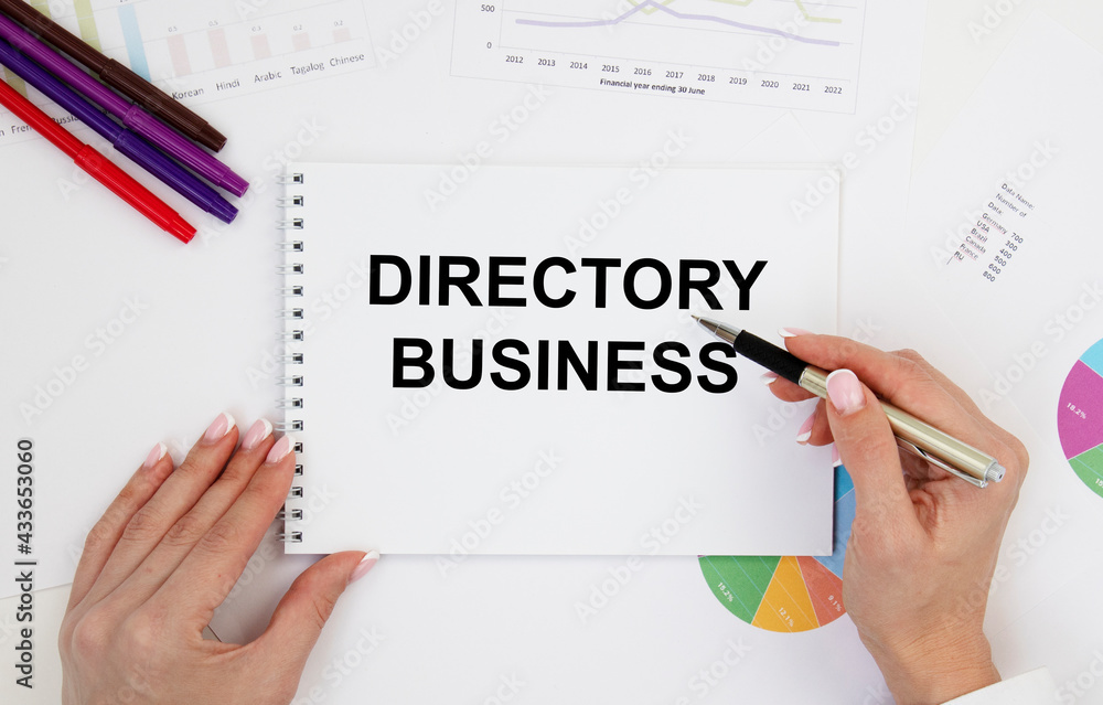 A girl holds a notebook with the text DIRECTORY BUSINESS, next to pencils, diagrams. A girl holds a notebook with the text DIRECTORY BUSINESS, next to pencils, diagrams.