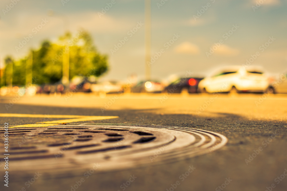 Summer in the city, the avenue with parked cars. Close up view of a hatch at the level of the asphalt Summer in the city, the avenue with parked cars. Close up view of a hatch at the level of the asphalt