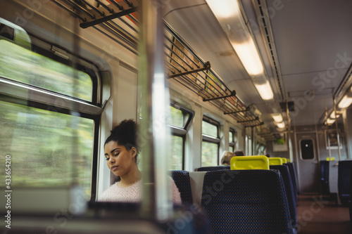 Mixed race woman in white sweater sleeping by window sitting on train photo