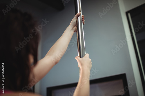 Caucasian woman exercising, holding on to metal pole at pole dance and fitness studio