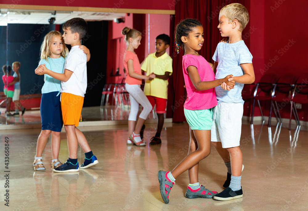 Group of happy positive childrens trying dancing with partner in classroom