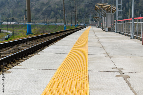 Empty platform of railway transport. The tactile paving of the track is yellow in perspective. The concept of a passenger platform at the train station.