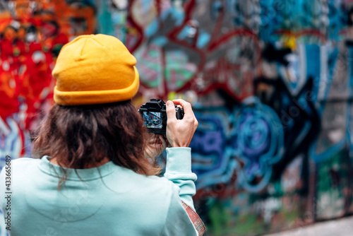 Back view of anonymous hipster male in knitted hat taking photo of graffiti wall on camera in city photo
