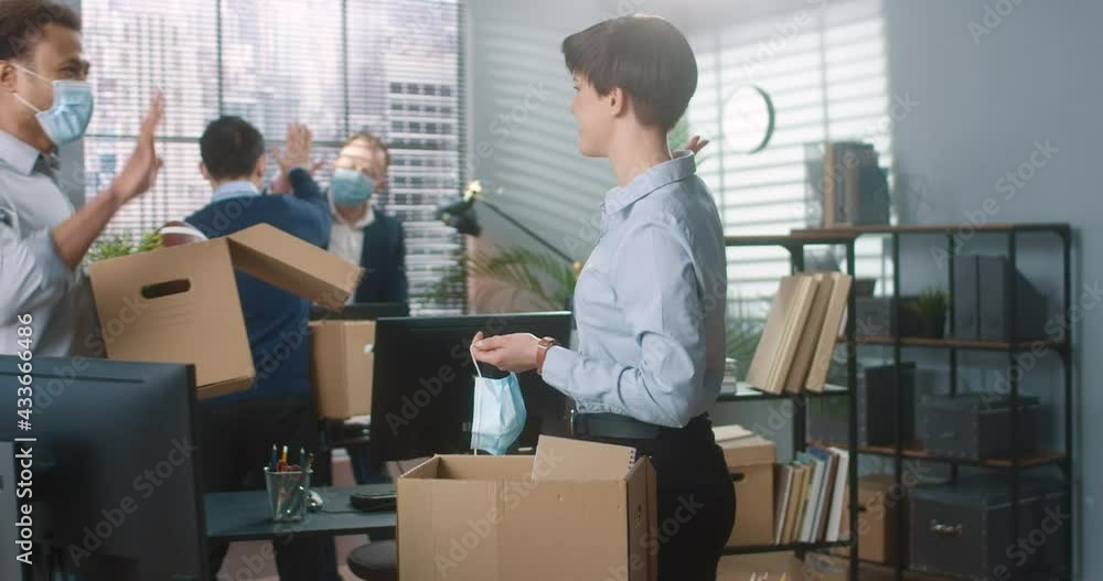 Mixed-races young people moving into new office during quarantine. Male and female workers with boxes in new cabinet. Woman removing medical mask from face unpacking stuff at workplace Mixed-races young people moving into new office during quarantine. Male and female workers with boxes in new cabinet. Woman removing medical mask from face unpacking stuff at workplace