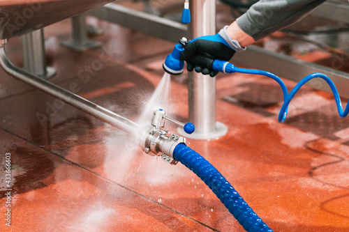 Crop unrecognizable male worker in mask washing valve of metal tank at work in brewing company photo