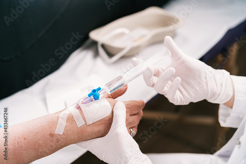Crop unrecognizable medic in latex gloves injecting remedy into arm of patient through intravenous catheter in hospital